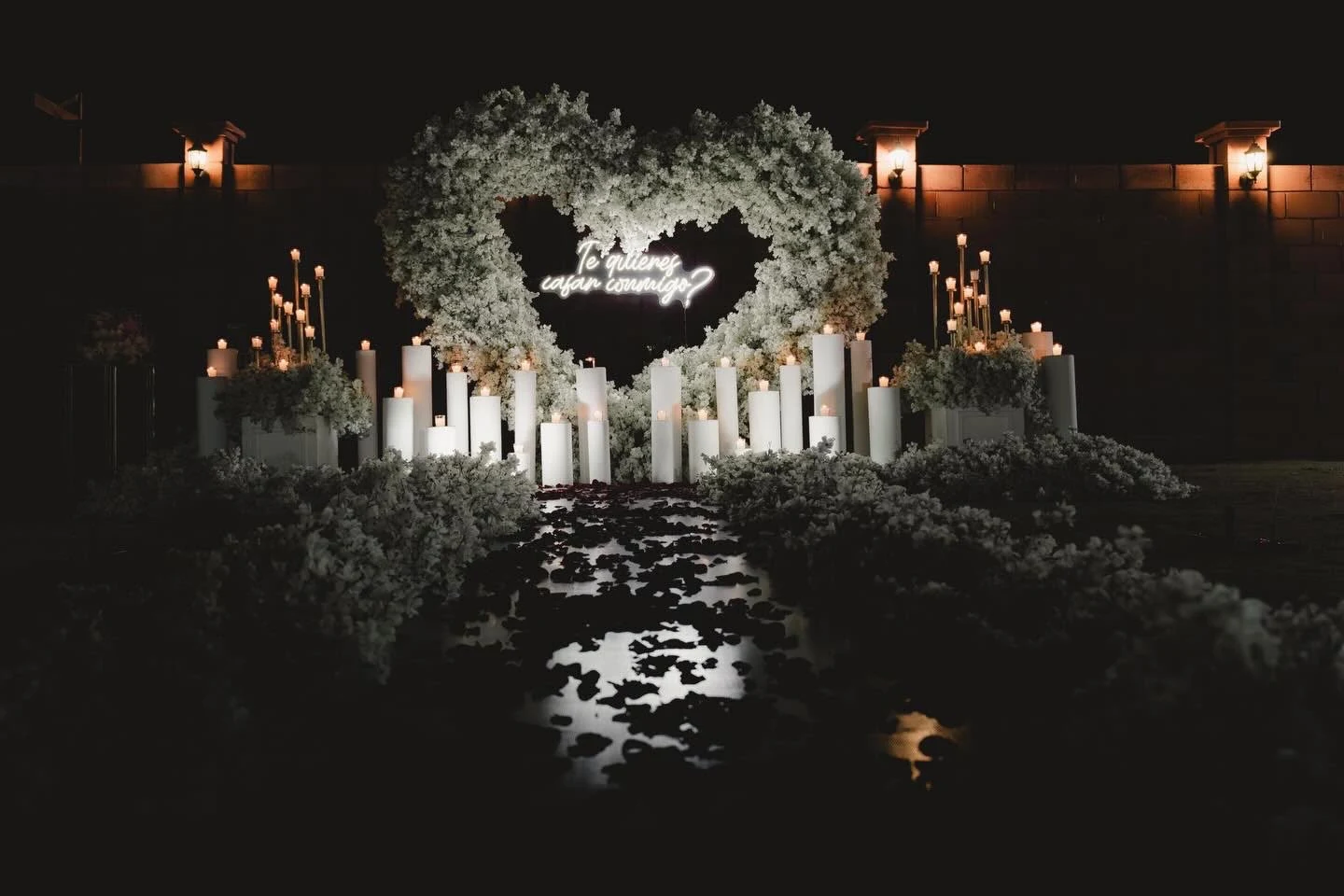 Fotografía real de una pedida de mano, con corazón floral y velas al aire libre